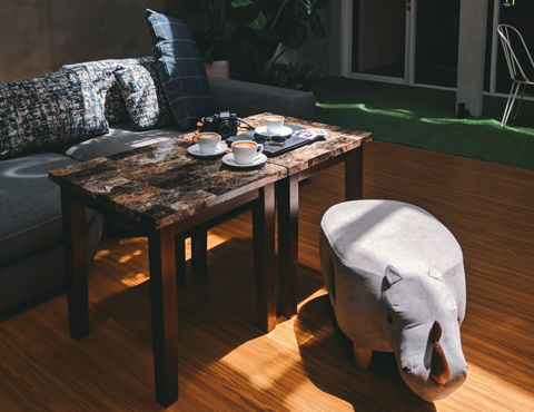 Outdoor couch, wooden tables with cups of coffee on them, and a gray hippopotamus chair