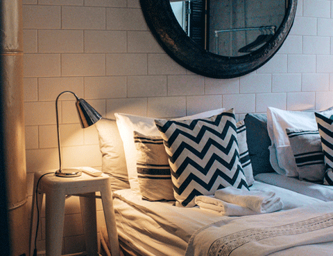 Close-up of a hotel room bed with light-colored sheets and blankets and nightstand with the light on