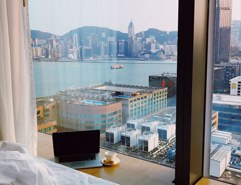 Hotel room with a view of a city, river, and mountains and laptop on the window ledge